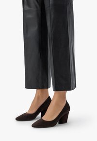 Ruskeat mokkasaappaat korolla, joissa on terävä kärki ja paksu korko, yhdistettyinä mustiin nahkasiipiin.