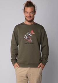 Olijfgroene sweatshirt met lange mouwen en een ronde hals. Heeft een illustratie van een beer met een rode hoed die op een fiets rijdt, vergezeld van tekst.