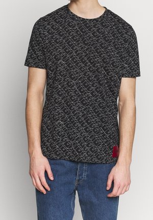 Schwarzes T-Shirt mit einem geometrischen weißen Muster, Rundhalsausschnitt, kurzen Ärmeln und einem roten Akzentetikett am Saum. Aus Baumwolle, lässige Passform.