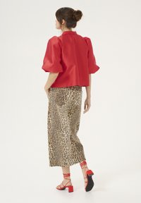 Red satin short-sleeve top with puffed sleeves, paired with a leopard print midi skirt. Features strappy red heeled sandals.