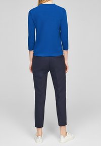 Blå texturerad stickad topp med trekvartslånga ärmar, som finns i kombination med marinblå slim fit-byxor. Ljusfärgade sneakers fulländar outfiten.