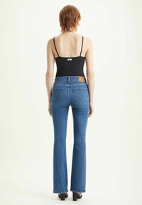 Jeans flared blu con vita media e tasche posteriori sottili. Presentano un'etichetta in pelle marrone sul cinturino e una superficie liscia.