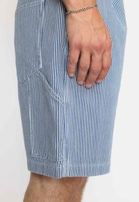 Blauwe en witte gestreepte shorts van stof met een textuurafwerking; heeft zijzakken en zichtbare stiksels langs de naden.