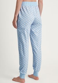 Blauwe pyjamabroek met polka dots, een lichtblauwe tailleband en manchetten. Zachte stof, taps toelopende pijpen, met grote witte stippen.