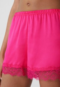 Felle roze shorts van gladde stof, met een kantafwerking aan de zoom met een ingewikkeld bloemmotief en een elastische tailleband.