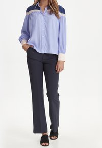 Jasnoniebieska koszula z długim rękawem, z akcentami w kolorze granatowym i kremowym, z plisowanymi detalami. W połączeniu z granatowymi spodniami i czarnymi mule na obcasie.