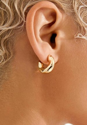 Kuldne rõngaskõrvarõngas siledapinna ja läikiva viimistlusega, millel on asümmeetriline disain, mis ümbritseb kõrvatagust.