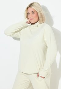 Helles beige Langarmshirt mit hohem Kragen, gerippter Textur und weißem Berglogo. Es hat eine lockere Passform und lange Ärmel mit Daumenlöchern.