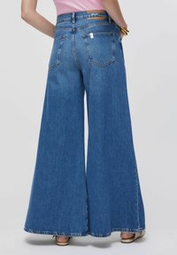Jean denim bleu à jambes larges avec une taille haute, présentant un ourlet brut, deux poches arrière, et une étiquette de marque marron sur la ceinture.