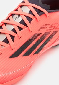 Svetlucne ružičaste nogometne kopačke s crnim akcentima, teksturiranom površinom i vezanjem na mekanom gornjem dijelu. Sadrži detalj "SPRINTGRID" sa strane.