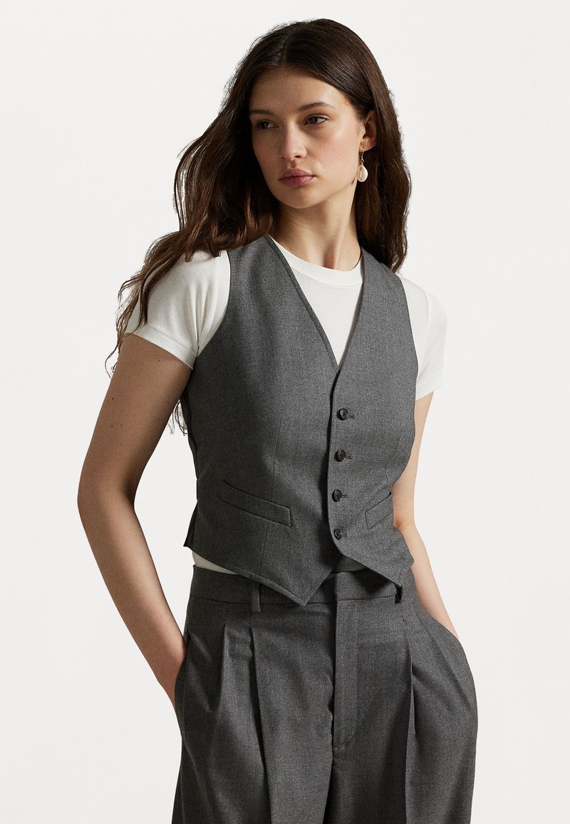 Vesta gri cu o croială adaptată, decolteu în V, cu cinci butoni în față și două buzunare laterale, asortată cu un tricou alb și pantaloni gri care se potrivesc.