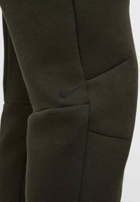 Pantalones deportivos verdes oscuros hechos de una tela suave, con un diseño elegante, costuras visibles y un sutil logo de Nike en el lateral.