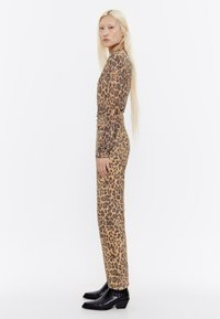 Leopardprint lange mouw jurk met een getailleerde pasvorm; rekbare stof. Gekocht met zwarte gestructureerde enkellaarzen en een natuurlijke achtergrond.