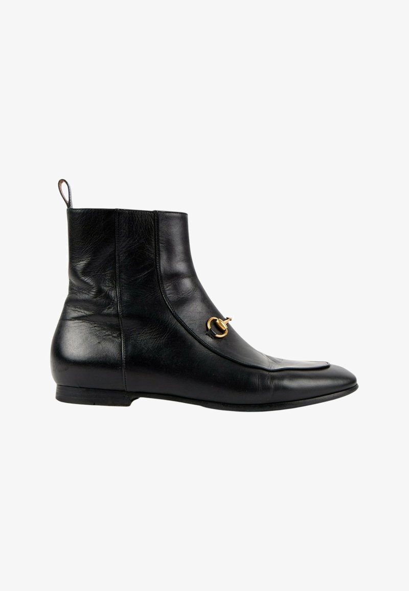 Bottine noire en cuir avec un petit détail en métal doré en forme de mors de cheval sur le côté et un talon plat et bas.