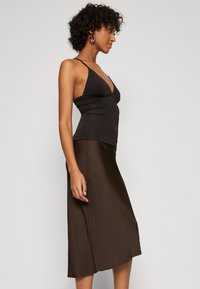 Robe en satin marron avec un corsage ajusté et une jupe évasée. Dotée de bretelles spaghetti et d'une fente sur le côté, offrant une texture lisse et une silhouette épurée.