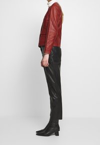 Röd läderjacka med en strukturerad design, kombinerad med svarta läderbyxor och spetsiga ankelstövlar. Sl ät textur och figursydd siluett.