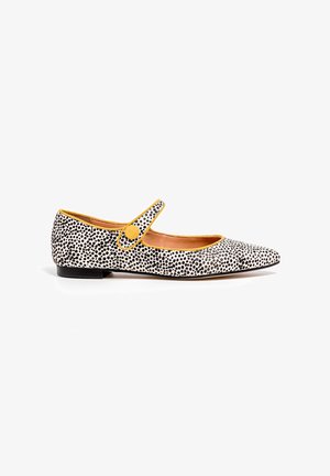Zapato plano de lunares en blanco y negro con puntera puntiaguda, acento amarillo alrededor de la abertura y una correa con cierre de botón redondo.
