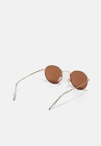 Ochelari de soare rotunzi cu lentile maronii, ramă din metal auriu, suporturi nazale transparente și brațe subțiri din argint. Design minimalist, fără embellishments suplimentare.