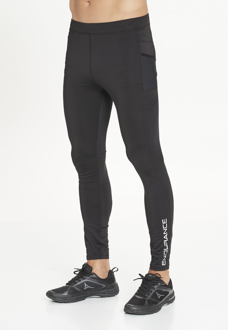 Manlig underkropp som bär svarta åtsittande leggings med sidoficka och texten "ENDURANCE" på vaden, i kombination med svarta sportskor.