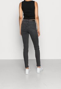 Jeans skinny negros de talle alto con un diseño de cinco bolsillos, detalles de costura sutiles y un ajuste elegante, combinados con zapatillas deportivas blancas de plataforma.