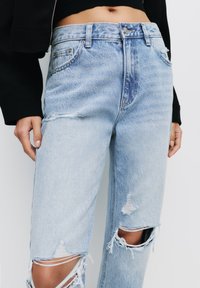Jeans in denim azzurro chiaro con effetto usurato, caratterizzati da una vita alta, cuciture visibili e strappi evidenti alle ginocchia e alle tasche.