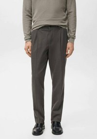 Sive hlače s pregibi, narejene iz gladkega blaga. Nositve z ustreznim svetlo sivim puloverjem in črnimi mokasini.