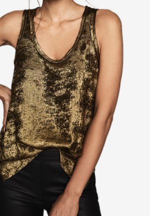 Débardeur sans manches en métal doré avec un décolleté plongeant porté avec un pantalon noir, présentant une coupe légèrement ample.