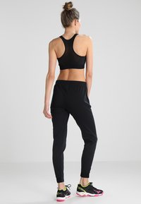 Reggiseno sportivo nero, realizzato in un tessuto testurizzato, abbinato a pantaloni jogger neri con vita elastica e scarpe da ginnastica nere con accenti rosa.