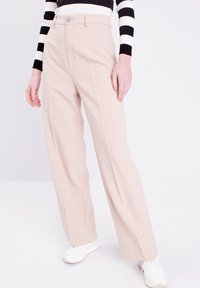 Pantaloni a gamba larga in un tessuto beige chiaro con una superficie liscia, dotati di chiusura frontale con zip e bottone, senza motivi visibili.