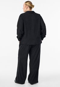 Černý kordový outfit zahrnující dlouhý rukáv s knoflíky a široké kalhoty, obojí s texturovaným povrchem a volným střihem.