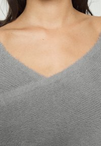 Grijze gebreide top met een zachte, fluffy textuur, een V-halsontwerp en schuin aangebrachte stoffen overlays.
