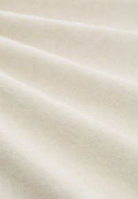Nahaufnahme von glattem, weichem cremefarbenem Stoff mit sanften Falten, die seine feine Textur und das gleichmäßige Strickmuster betonen.