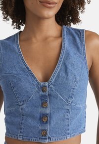 Gekürzter Denim-Weste in Hellblau mit V-Ausschnitt, fünf Holzknöpfen und vertikalen Nähten vorne. Besitzt eine glatte Textur.