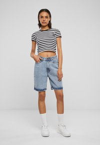 Un crop top rayé noir et blanc associé à un short en denim bleu clair. La tenue présente une coupe décontractée et est complétée par des baskets blanches.