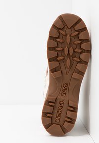 Podeszwa brązowego botka Michael Kors z głębokim bieżnikiem i geometrycznymi wzorami, umieszczona na białym tle w rogu.