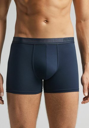 Marineblaue Boxerbriefs aus glattem Stoff. Breiter elastischer Bund mit Branding, der über eine konturierte Tasche und kurzen Beinlängen verfügt.