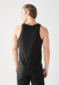 Top negro sin mangas, confeccionado en tejido suave. Presenta un escote redondeado y un corte holgado, combinado con pantalones negros.