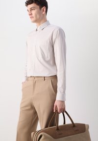 Lightly striped beige and white long-sleeve shirt, paired with tan trousers. Holding a brown leather accented duffel bag.