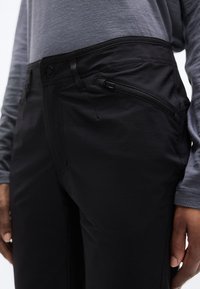 Μαύρο παντελόνι με λεία υφή, λεπτομέρεια τσέπης με φερμουάρ στο πλάι και εφαρμοστό ζωνάκι. Συνδυασμένο με γκρι μπλούζα μακρυμάνικη.