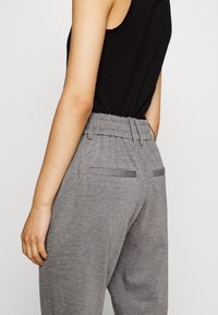 Pantaloni con cintura elastica grigia in tessuto texturizzato, con due tasche posteriori e vestibilità affusolata, abbinati a una canotta nera.