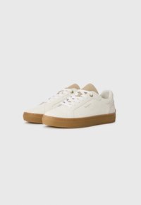 Hvite skinn sneakers med beige detaljer, rund tå, gulllogo, flatt brunt gummisåle, og hvite snøringer. Teksturerte sidepaneler forbedrer designet.