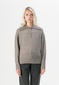 Brązowy sweter z wełny z zapięciem na guziki i ściągaczem, z długimi rękawami i luźnym krojem, w zestawie z szarymi spodniami.