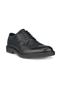 Chaussure brogue en cuir noir avec design à bouts ailés, détails perforés et lacets noirs, sur fond blanc.