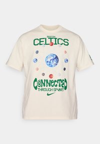 Kremfarget bomulls t-skjorte med teksten "BOSTON CELTICS" i grønt, grafikk av jorden, planeter og "CONNECTED THROUGH SPORT" i grønt.