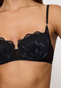 Schwarzer Spitzen-BH mit gewellten Rändern, verziert mit floralem Stickerei in Dunkelblau, dünnen verstellbaren Trägern und einem glatten Unterband.