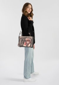 Borsa a spalla nera e grigia con un design a cartone animato fantasioso, dotata di chiusura a zip e tracolla regolabile. Tessuto liscio e strutturato.