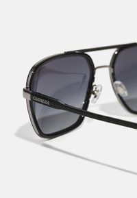 Occhiali da sole neri con montatura texture e lenti scure. Caratteristiche includono un evidente logo Carrera sul lato e naselli per il comfort.
