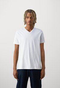 T-shirt en coton blanc à col en V avec des manches courtes, présentant une surface légèrement texturée et une coupe décontractée, associé à un pantalon en denim bleu foncé.