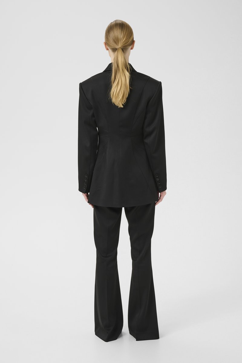 Black tailored suit with structured shoulders, single-breasted jacket, and flared pants. Smooth fabric with subtle seams and button details.