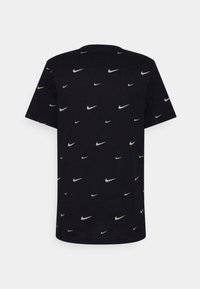 Sort bomulds-T-shirt med kortærmer, der har et gentaget mønster af små Nike Swoosh-logoer i hvide, grønne og røde accenter.